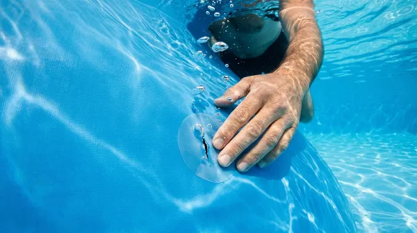 Application d'une rustine en PVC sous l'eau pour réparer une petite fuite de liner de piscine.
